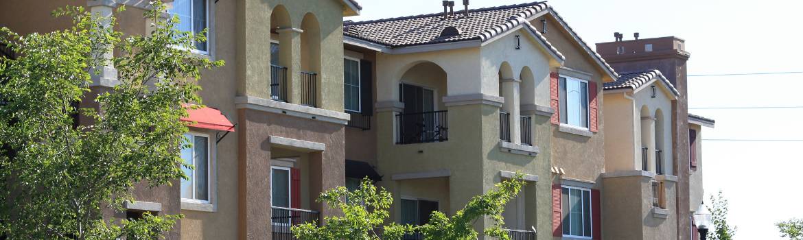 a three story apartment complex showing five balconies with trees just outside the complex on a sunny day