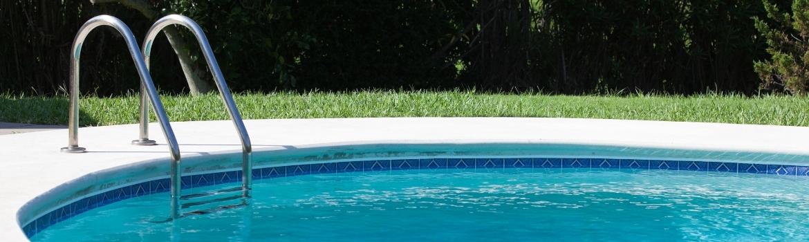 a swimming pool with a ladder going into the deep end with grass in a backyard