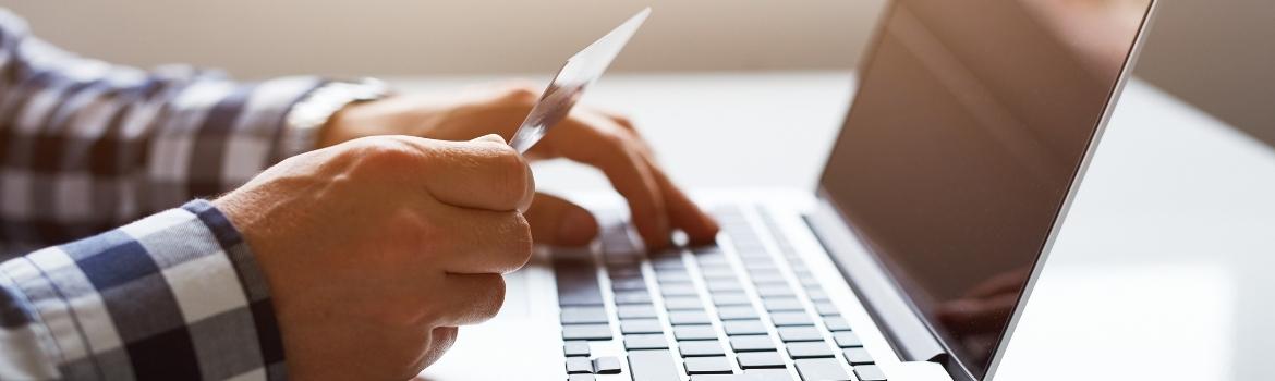 a person holding a credit card while typing on a laptop computer