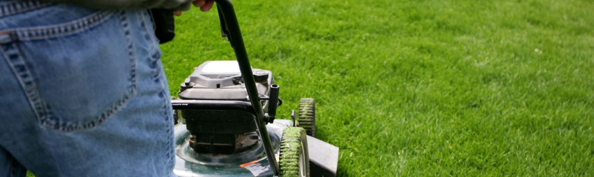 a close up of a man mowing the lawn with a push mower