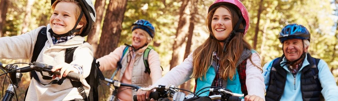 two females, ages seven and 14 are on mountain bikes with their grandparents right behind them also on mountain bikes in the forest.  