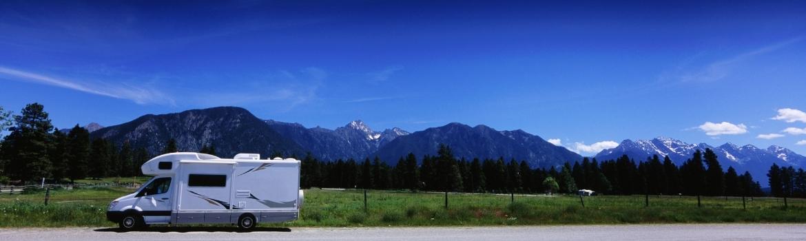 a small motorhome is pulled over on the side of the road and in the background is a blue sky with snow capped mountains