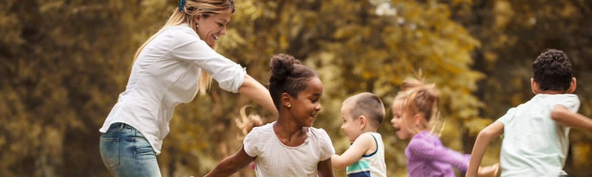 a mother plays with five children from various backgrounds and ages outdoor 