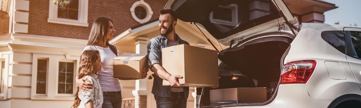 A male and female couple unload boxes from their small suv in the driveway of their house