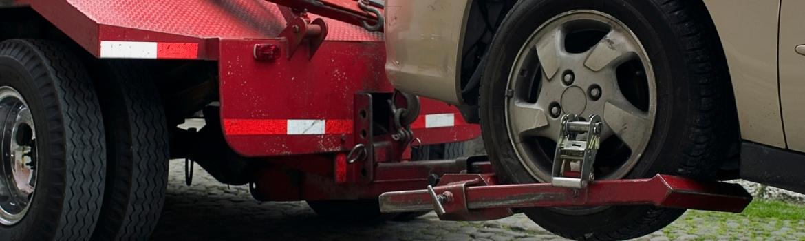 a red tow truck has a car lifted into the air by one set of tires while the other set of tires is presumably on the ground.