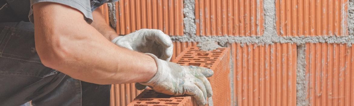 a man lays a brick on top of other bricks, with fresh mortar 