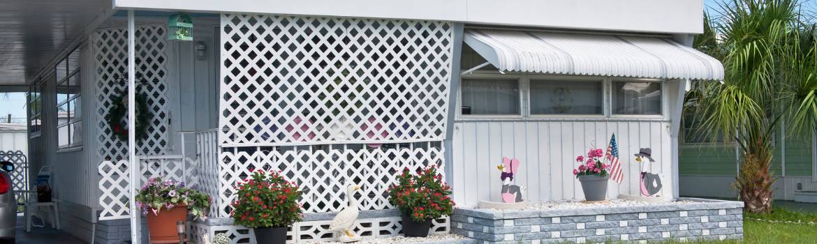 a white mobile home with  plants sitting on the brick wall and palm tree on the side yard